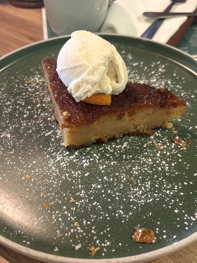 A slice of tart with cream on a dark green plate.