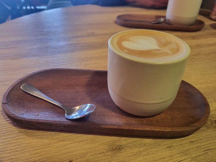 A latte with rosetta art in a cream cup on a wooden board.