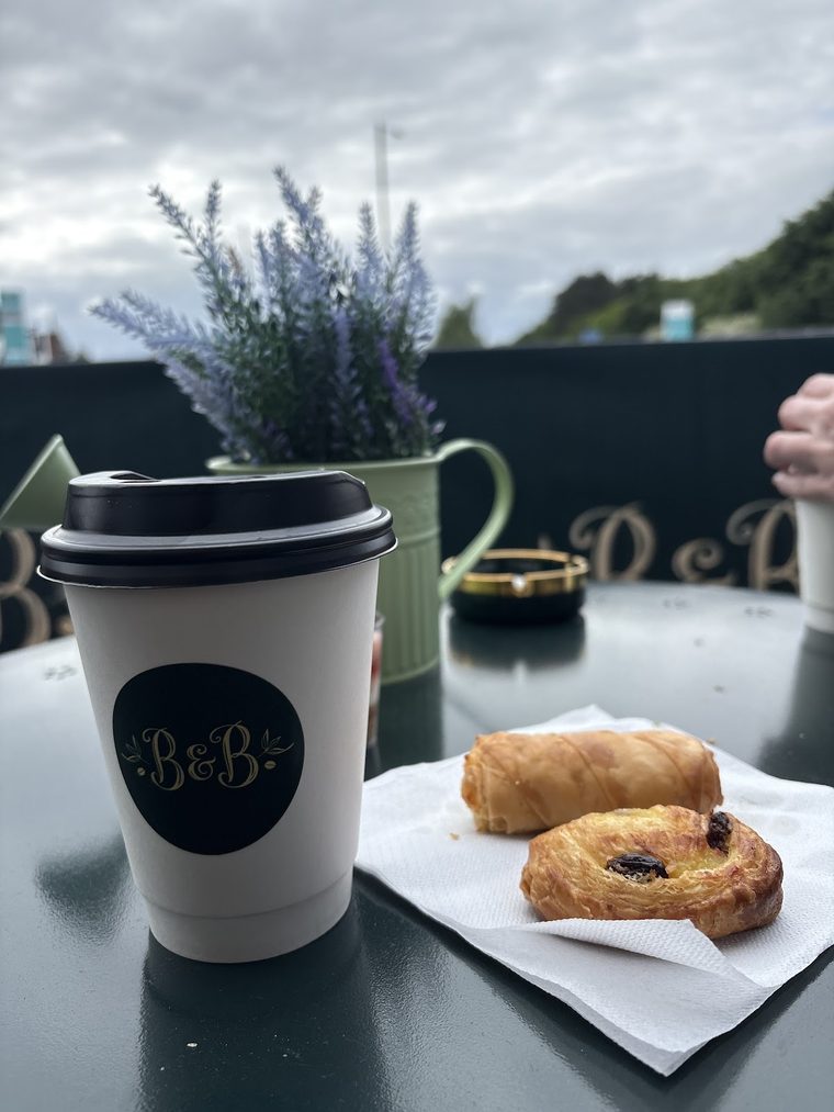 A pain au chocolat and a sausage roll on a napkin beside a takeaway coffee.