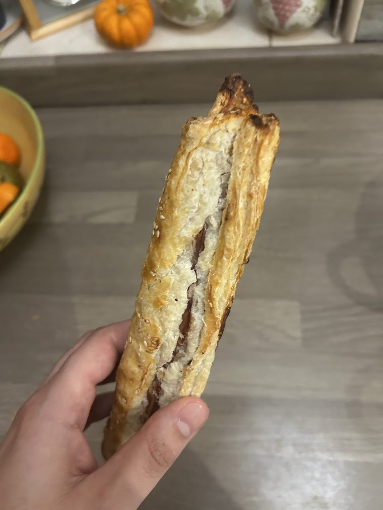 A long flaky filled pastry held up in front of the counter.