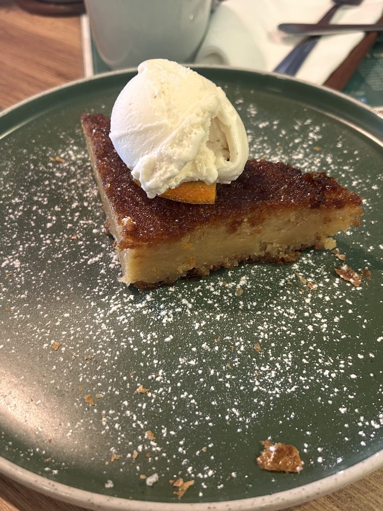 A slice of tart dusted with sugar, topped with cream, on a dark green plate.